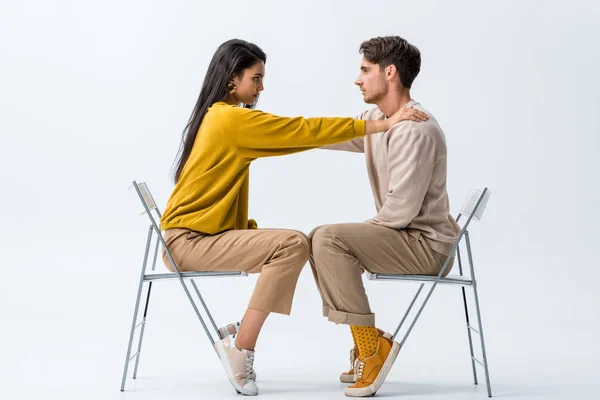 Seitenansicht eines attraktiven Mädchens, das auf einem Stuhl sitzt und den Mann auf Weiß berührt — Stockfoto