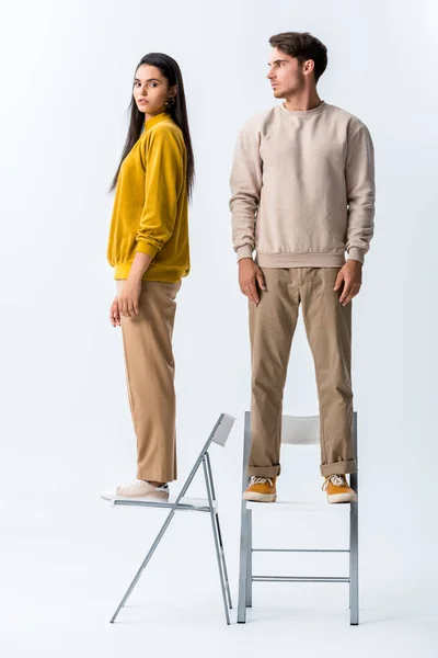 Handsome man standing on chair and looking at stylish girl on white — Stock Photo