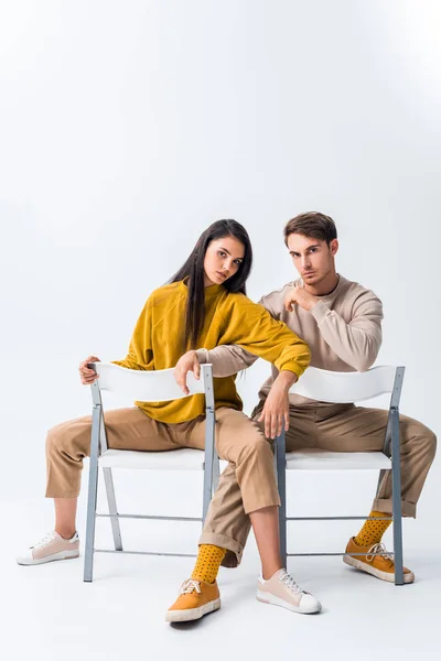 Bonito homem sentado na cadeira e posando com atraente menina no branco — Fotografia de Stock