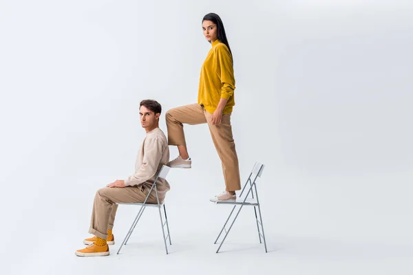 Stylish girl standing on chair near handsome man sitting on white — Stock Photo