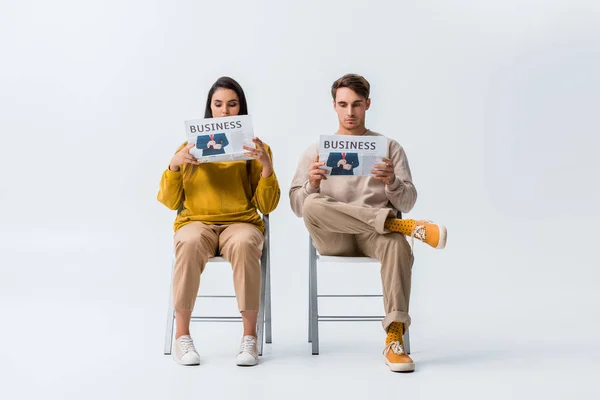 Woman and man sitting on chairs and reading business newspapers on white — Stock Photo