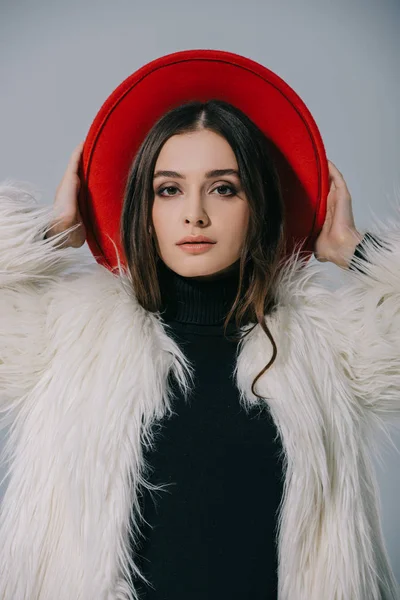 Mujer elegante de moda posando en abrigo de piel blanca y sombrero rojo, aislado en gris - foto de stock