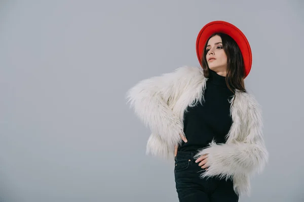 Atraente mulher elegante posando em casaco de pele branca e chapéu vermelho, isolado em cinza — Fotografia de Stock