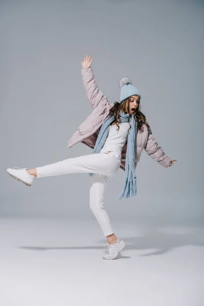 Bella ragazza elegante che balla in cappotto caldo, cappello a maglia e sciarpa su grigio — Foto stock