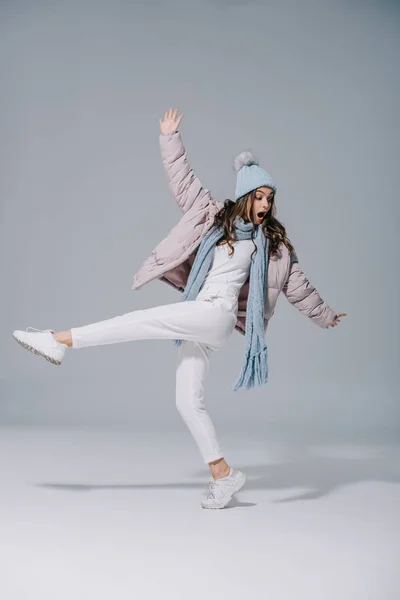 Hermosa chica elegante bailando en abrigo caliente, sombrero de punto y bufanda en gris - foto de stock