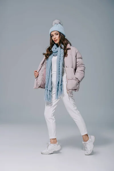 Attraente ragazza in posa in cappotto caldo, cappello a maglia e sciarpa su grigio — Foto stock