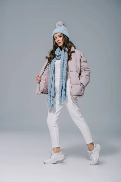 Attractive girl posing in warm coat, knitted hat and scarf on grey — Stock Photo