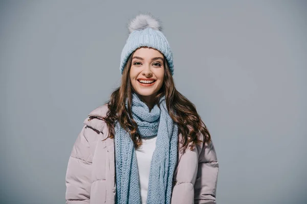Beautiful cheerful girl posing in warm coat, knitted hat and scarf, isolated on grey — Stock Photo