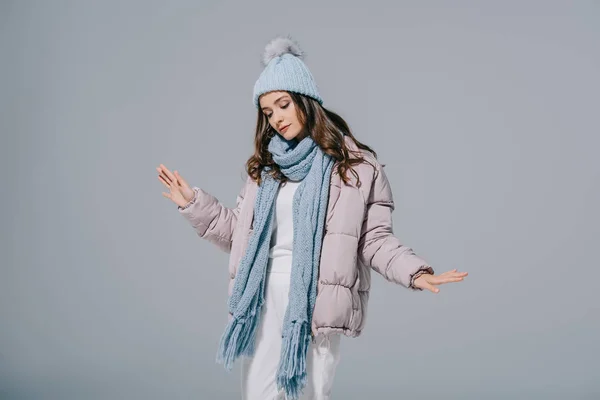 Hermosa chica bailando en abrigo caliente, sombrero de punto y bufanda, aislado en gris - foto de stock