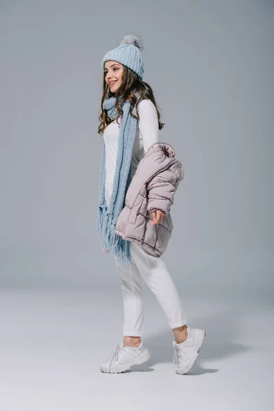 Attractive happy woman posing in trendy coat, knitted hat and scarf on grey — Stock Photo