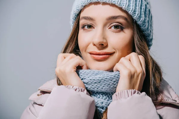 Красивая улыбающаяся девушка, позирующая в пальто, вязаной шляпе и шарфе, изолированная на сером — стоковое фото