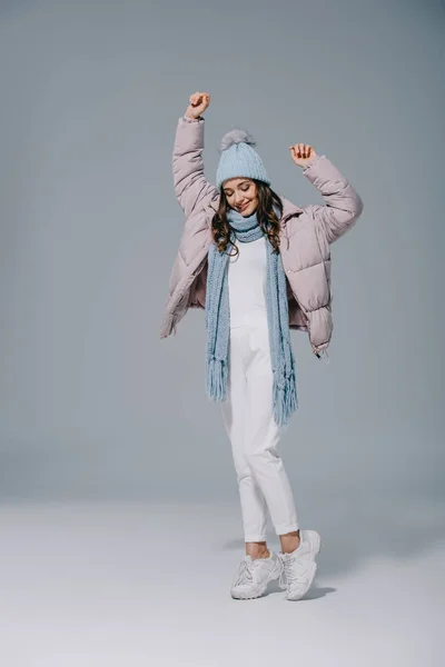 Schönes Mädchen tanzt in warmem Mantel, Strickmütze und Schal auf grau — Stockfoto
