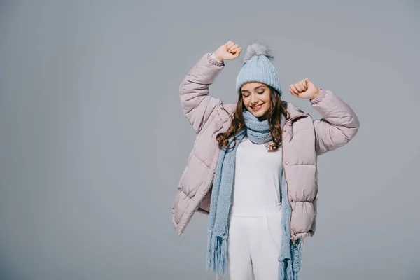 Attraente donna felice che balla in cappotto caldo, cappello e sciarpa in maglia, isolata sul grigio — Foto stock