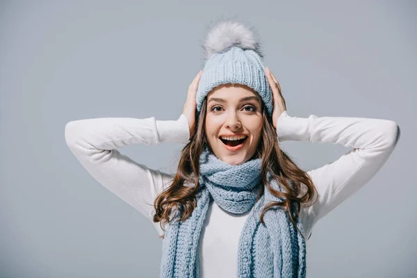 Aufgeregtes Mädchen posiert in blauer Strickmütze und Schal, isoliert auf grau — Stockfoto