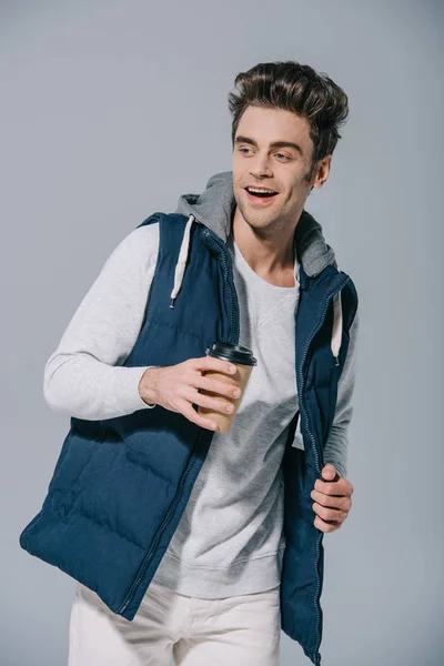 Uomo allegro in gilet caldo che tiene il caffè da andare, isolato su grigio — Foto stock