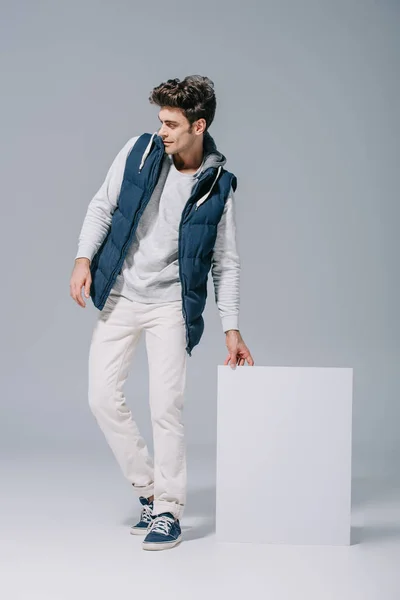 Schöner stylischer Mann in Weste posiert mit leerem Brett auf grau — Stockfoto