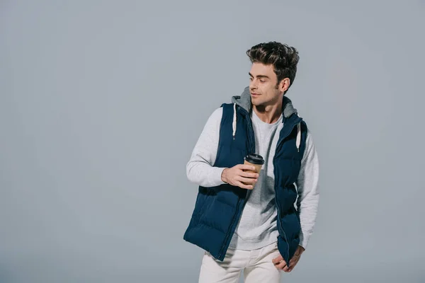 Handsome pensive man in warm waistcoat holding coffee to go, isolated on grey — Stock Photo