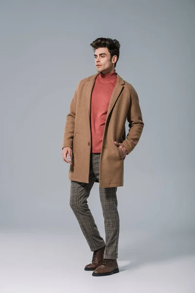 Красивый модный мужчина, позирующий в бежевом пальто на сером — стоковое фото