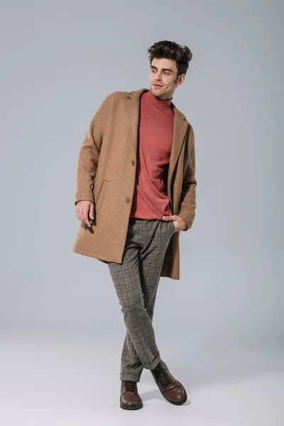 Beau modèle masculin posant en manteau beige élégant sur gris — Photo de stock