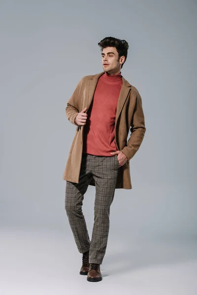 Модный молодой человек, позирующий в бежевом пальто на сером — стоковое фото