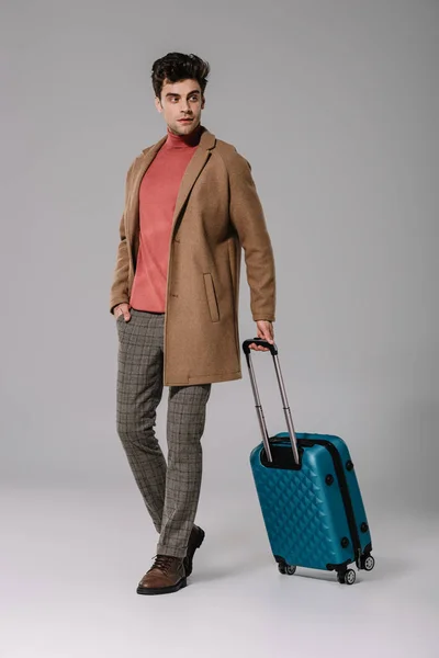 Stylischer Mann posiert in beigem Mantel mit Reisetasche auf grau — Stockfoto