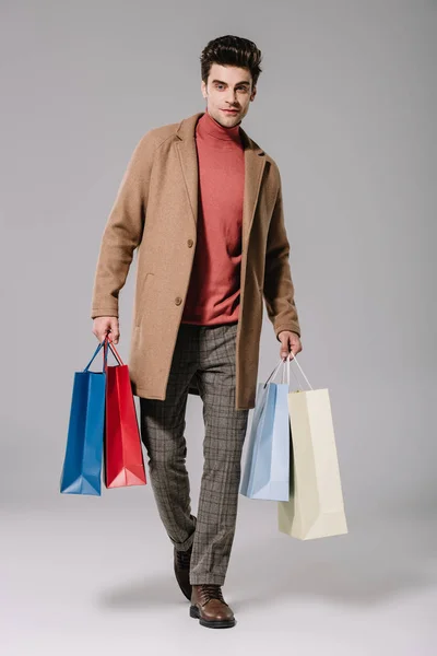 Stylish man in beige coat holding shopping bags on grey — Stock Photo