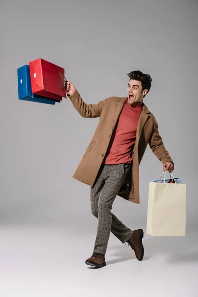 Excited stylish man in beige coat walking with shopping bags on grey — Stock Photo