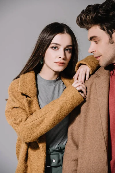 Модная пара, позирующая в бежевых пальто, изолированная на сером — стоковое фото