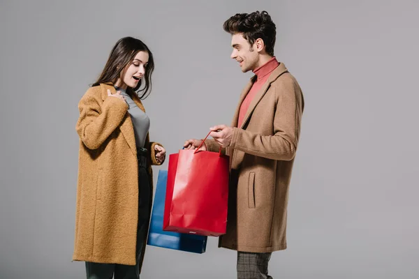 Excited couple in beige coats posing with shopping bags isolated on grey — Stock Photo