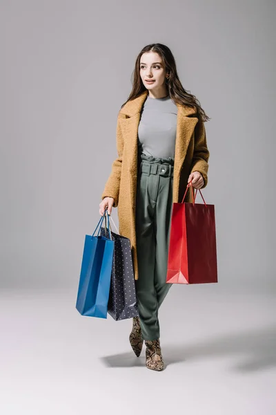 Fashionable elegant woman in beige coat holding shopping bags on grey — Stock Photo