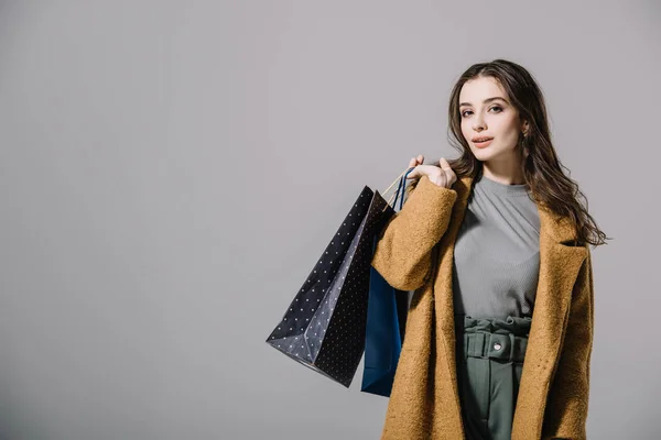 Señora de moda en abrigo beige sosteniendo bolsas de compras, aislado en gris - foto de stock
