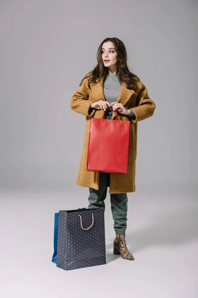 Fille à la mode en manteau beige tenant des sacs à provisions sur gris — Photo de stock