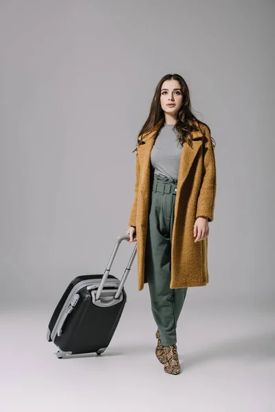 Hermosa mujer elegante en abrigo beige caminando con con bolsa de viaje en gris - foto de stock