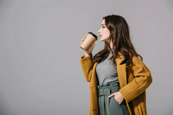 Bella donna in cappotto beige bere caffè per andare, isolato su grigio — Foto stock