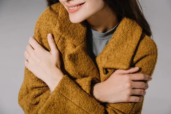 Cropped view of smiling girl posing in warm beige coat, isolated on grey — Stock Photo