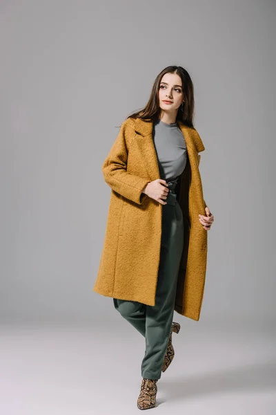 Привлекательная элегантная девушка позирует в бежевом пальто на сером — стоковое фото