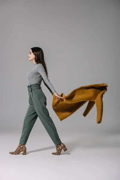 Stylish elegant girl taking off beige coat on grey — Stock Photo