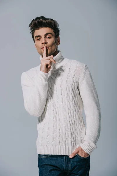 Happy man in white knitted sweater showing silence symbol, isolated on grey — Stock Photo