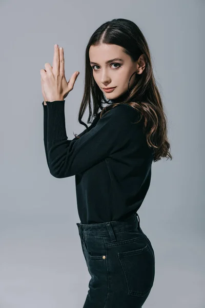 Attractive fashionable girl in black sweater showing hand gun, isolated on grey — Stock Photo