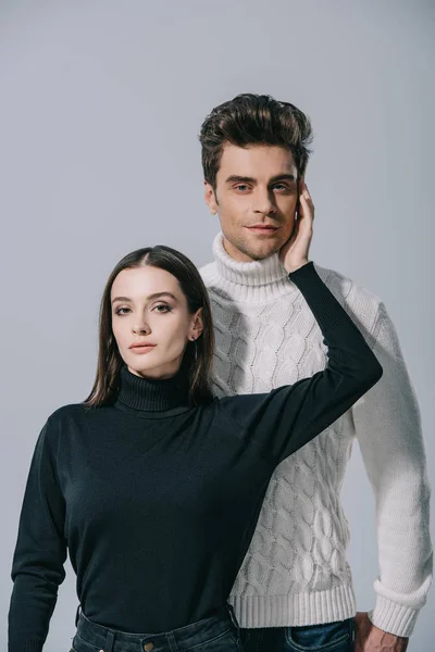 Модна пара позує в білих і чорних осінніх светрах, ізольована на сірому — стокове фото