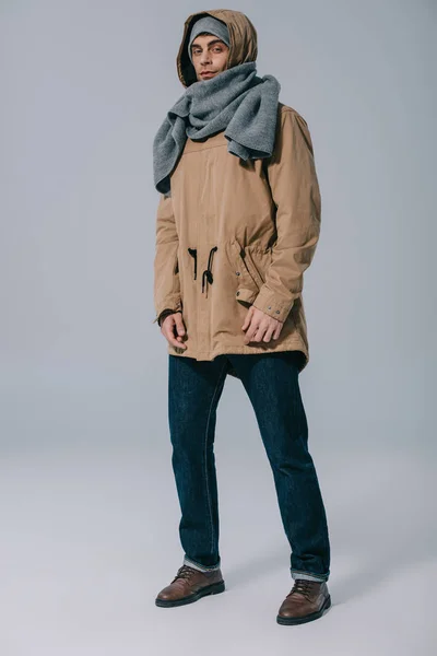 Guapo elegante hombre posando en sombrero, bufanda y abrigo en gris — Stock Photo