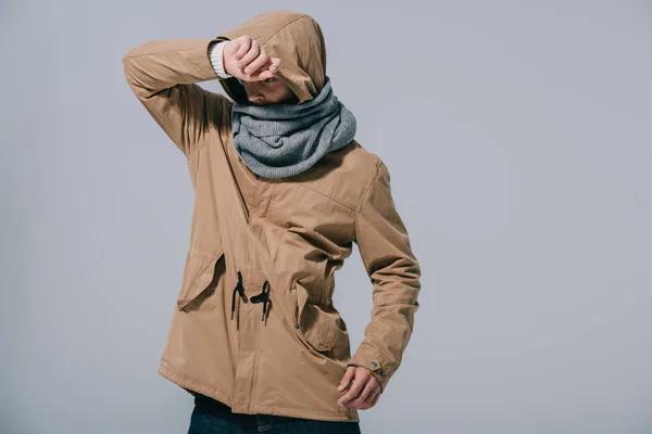 Jeune homme posant en écharpe, manteau et capuche, isolé sur gris — Photo de stock