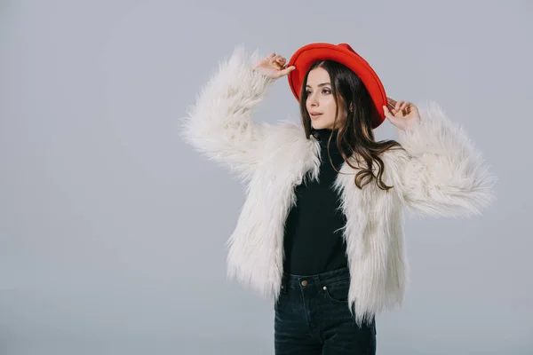 Atractiva chica elegante posando en abrigo de piel blanca y sombrero rojo, aislado en gris - foto de stock