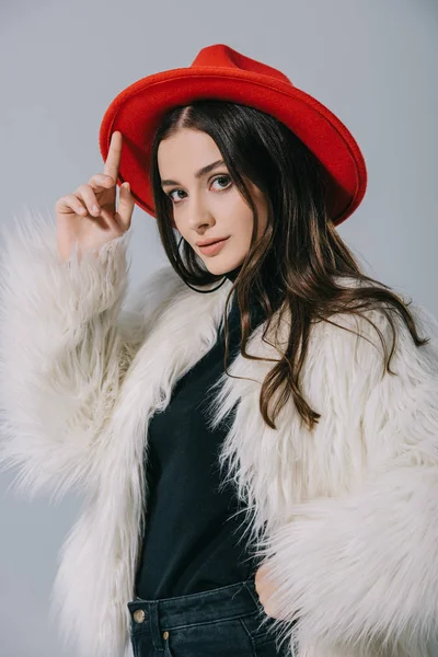 Модная элегантная девушка позирует в белом шубе и красной шляпе, изолированные на сером — стоковое фото