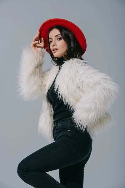 Modello elegante in posa in pelliccia bianca e cappello rosso, isolato su grigio — Foto stock