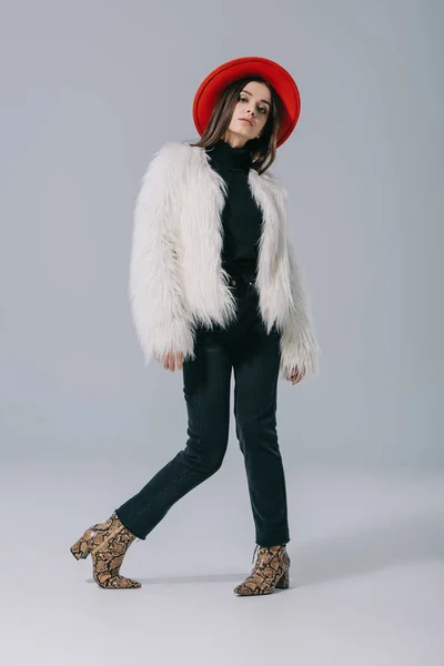 Stylish elegant woman posing in white fur coat and red hat on grey — Stock Photo
