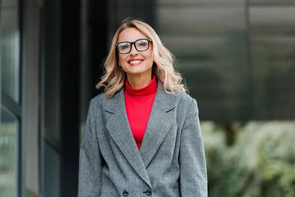 Attractive businesswoman in coat and glasses smiling and looking away — Stock Photo