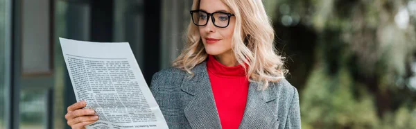 Colpo panoramico di attraente donna d'affari in cappotto e occhiali lettura giornale — Foto stock