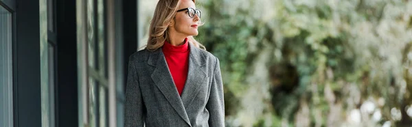 Plan panoramique de femme d'affaires attrayante en manteau et lunettes détournant les yeux — Photo de stock