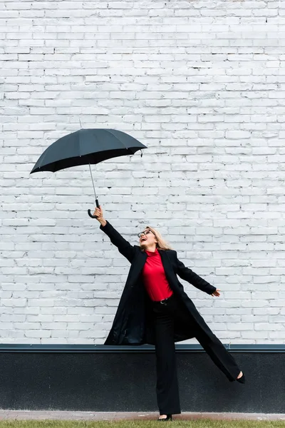 Attractive businesswoman in black coat smiling and holding umbrella — Stock Photo